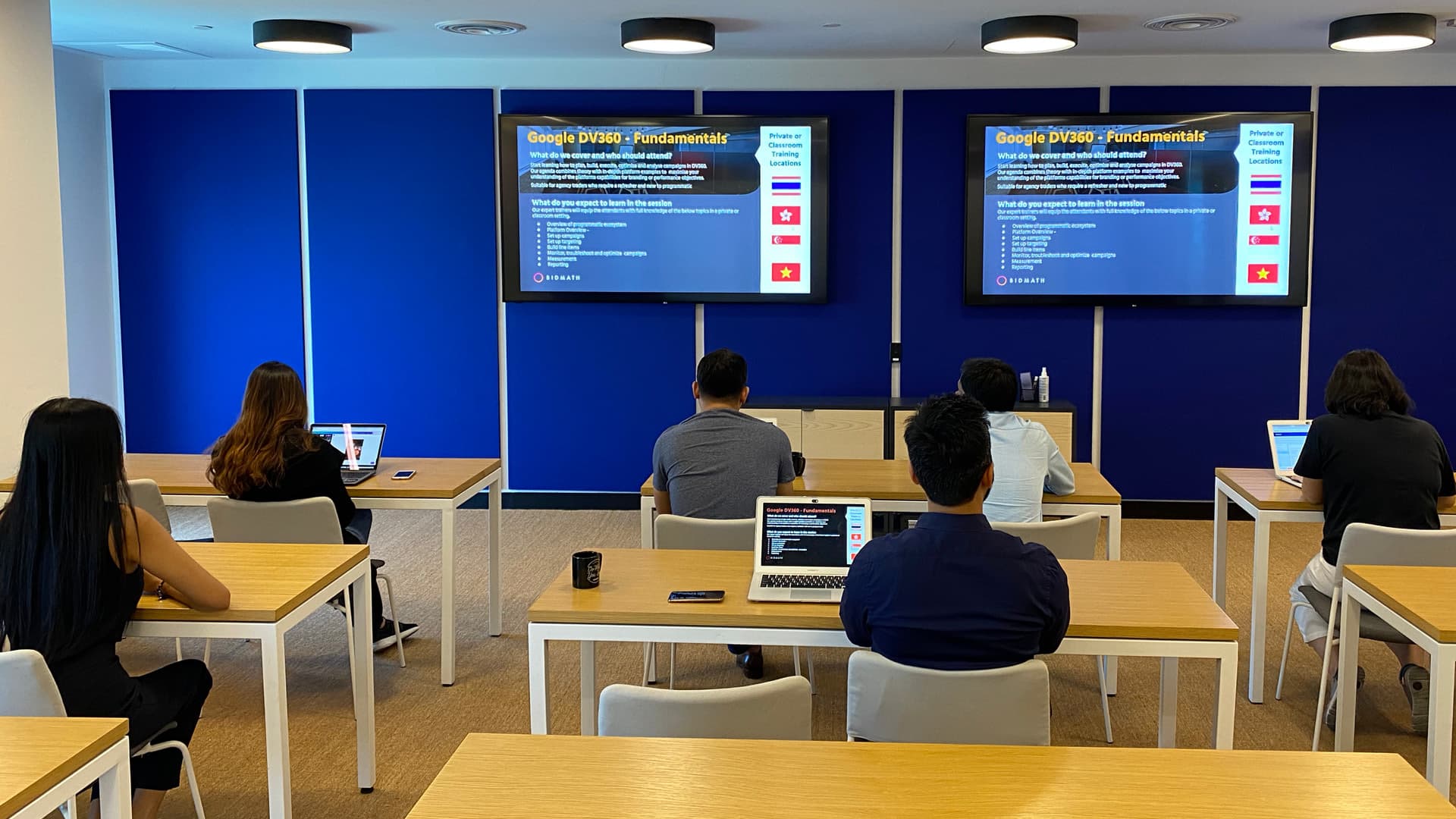 Attendees at desks facing two screens showing a Google DV360 fundamentals presentation